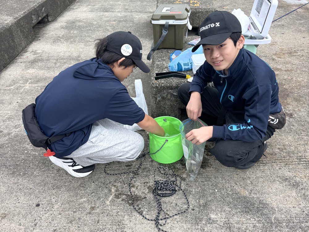並んでしゃがみ、バケツの前で準備をする部員2人