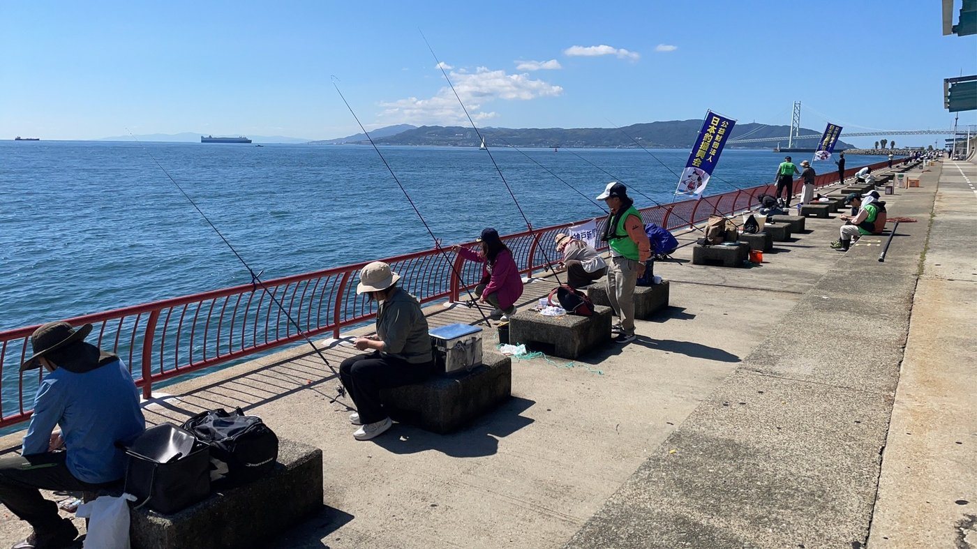 日本釣振興会ののぼりが並ぶ波止で、海に向かって竿を出す参加者
