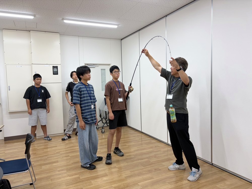 講師が竿先を持って曲がりを見せ、部員がリールを持つ